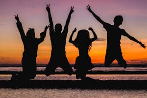 Silhouette of friends jumping on the beach at sunset, celebrating summer fun.